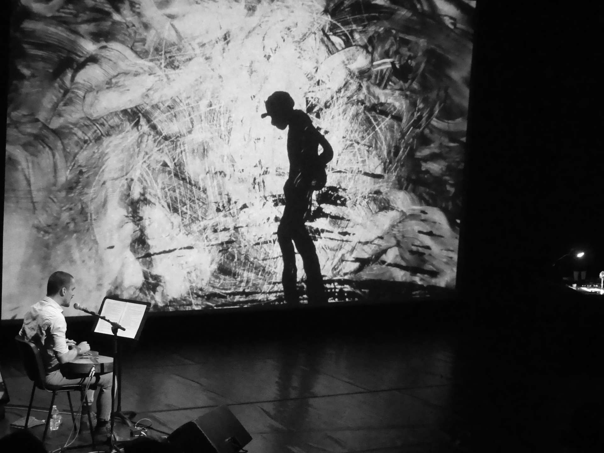 Un musicien devant un dessin projeté sur scène (noir et blanc).